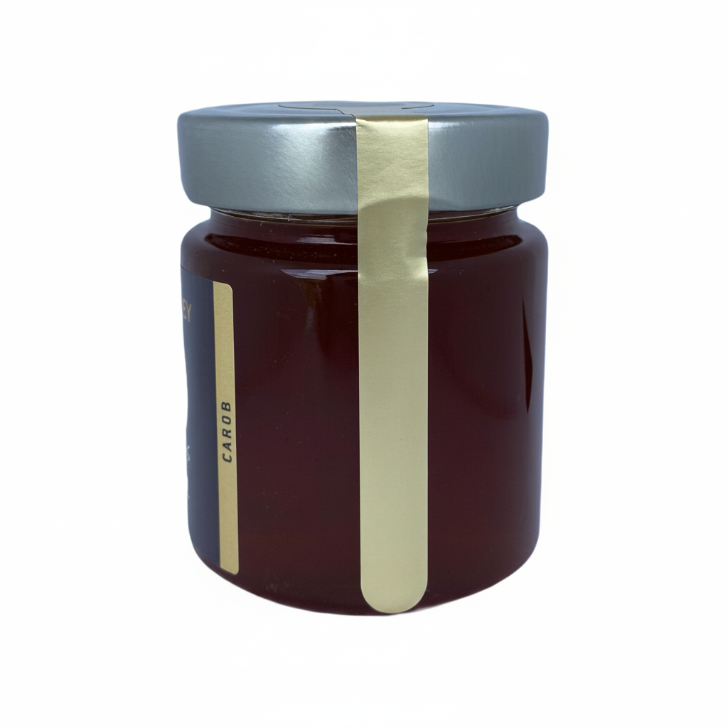 A glass jar of dark honey with a silver lid and a vertical gold seal, shown on a plain white background.