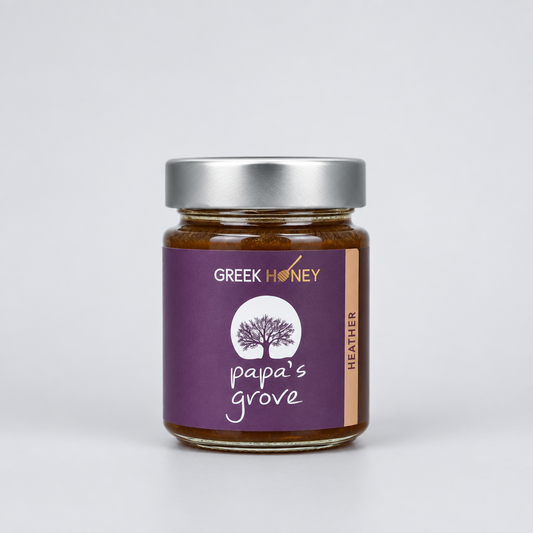 A glass jar of Greek Raw Heather Honey from Papa's Grove, featuring a purple label with a tree logo and a sliver metal lid, set against a neutral gray background.