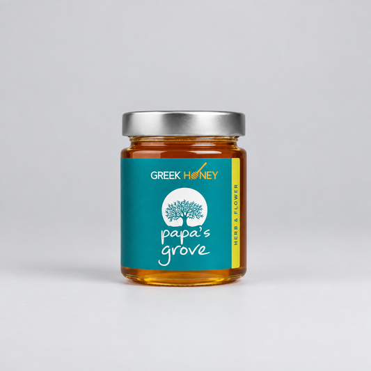 A glass jar of Greek Herb & Flower Honey from Papa's Grove, filled with golden honey and featuring a teal label with a tree logo, set against a neutral light gray background.