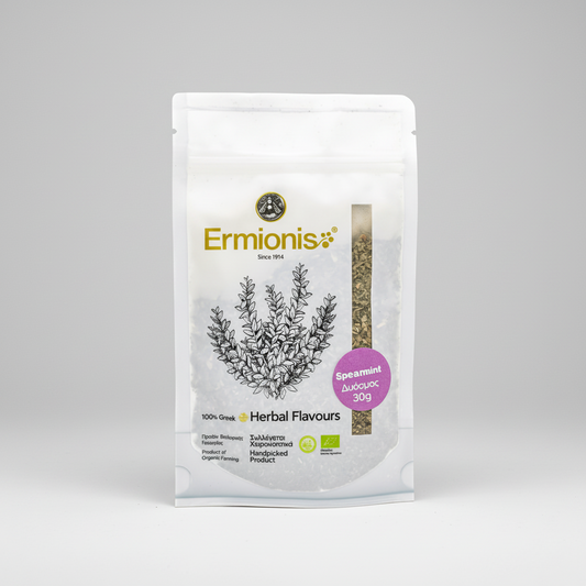 A 30g stand-up pouch of Ermionis Spearmint Organic herb, featuring a white background with a black botanical illustration and a purple circular badge, set against a neutral gray studio backdrop.