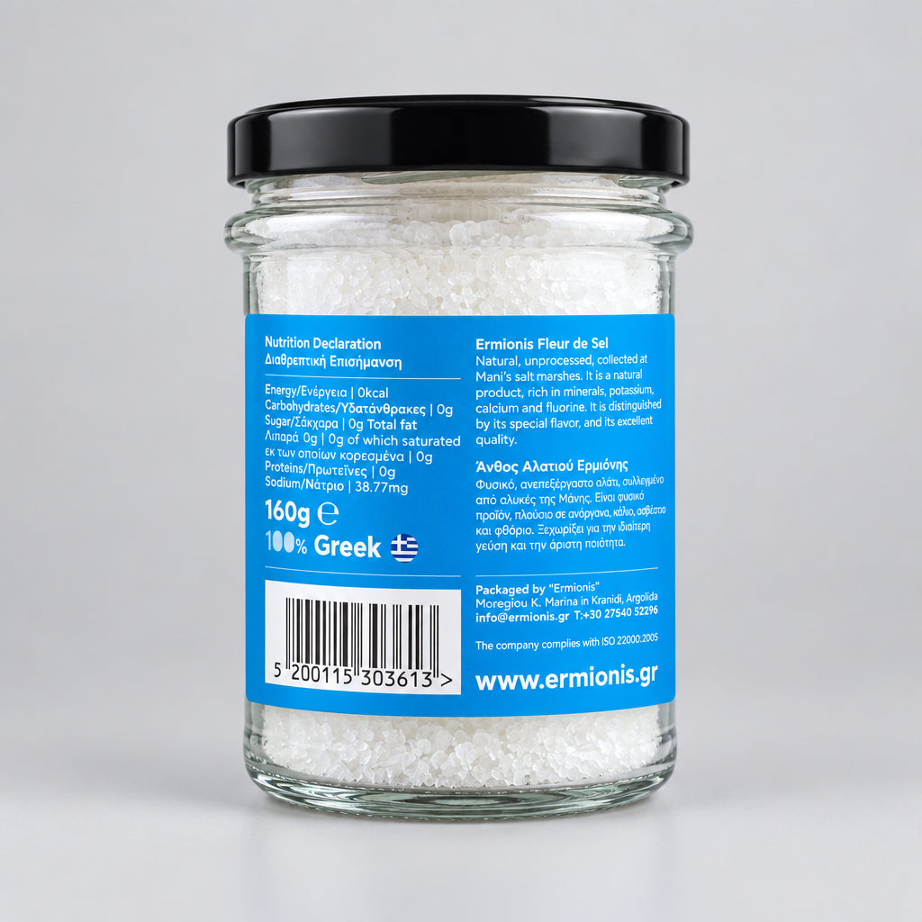 A glass jar of Greek Ermionis salt flakes with a black lid and a blue label, with a light grey background.
